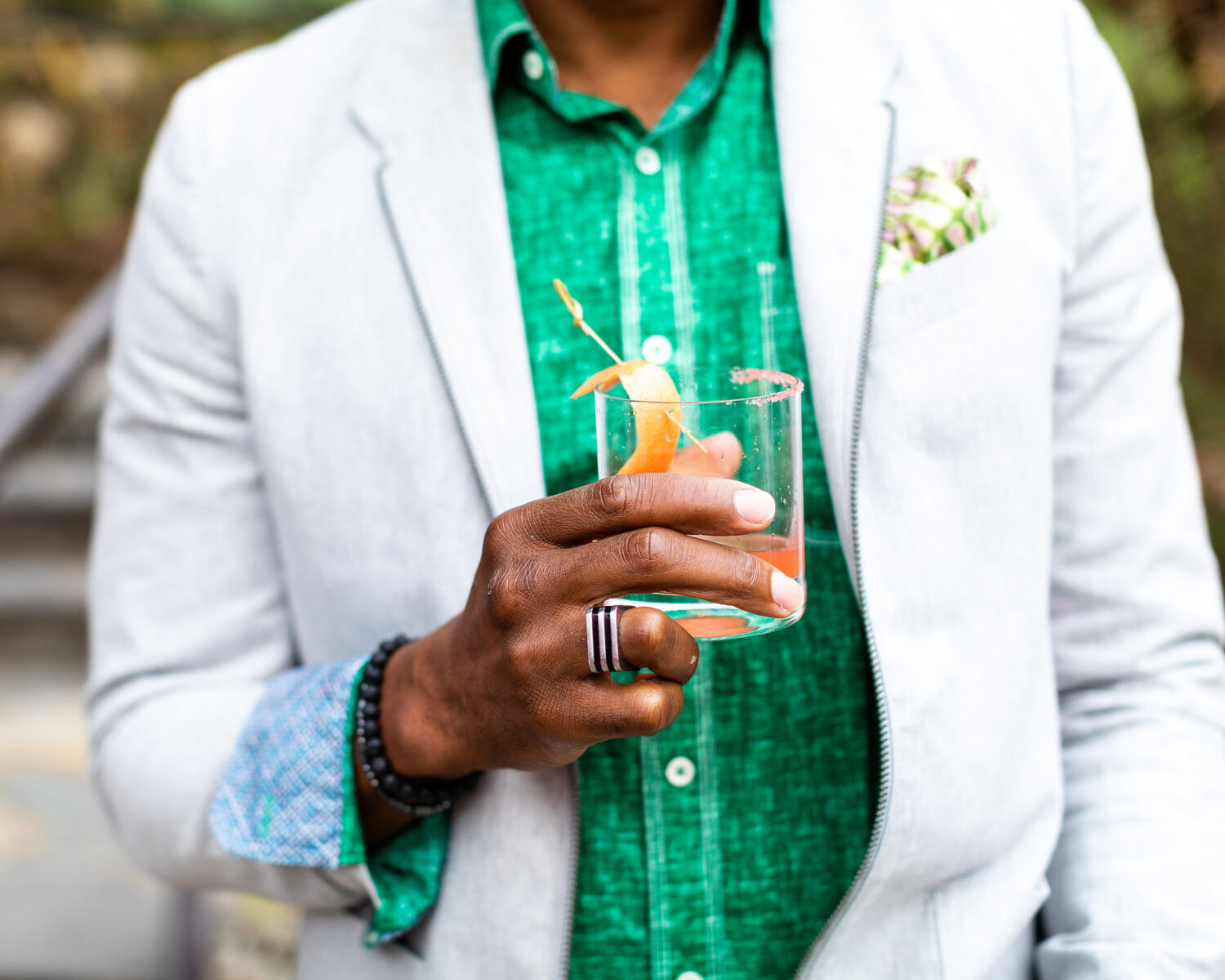 close up of a guest holding a colorful cocktail. Their shirt is a bright green color.