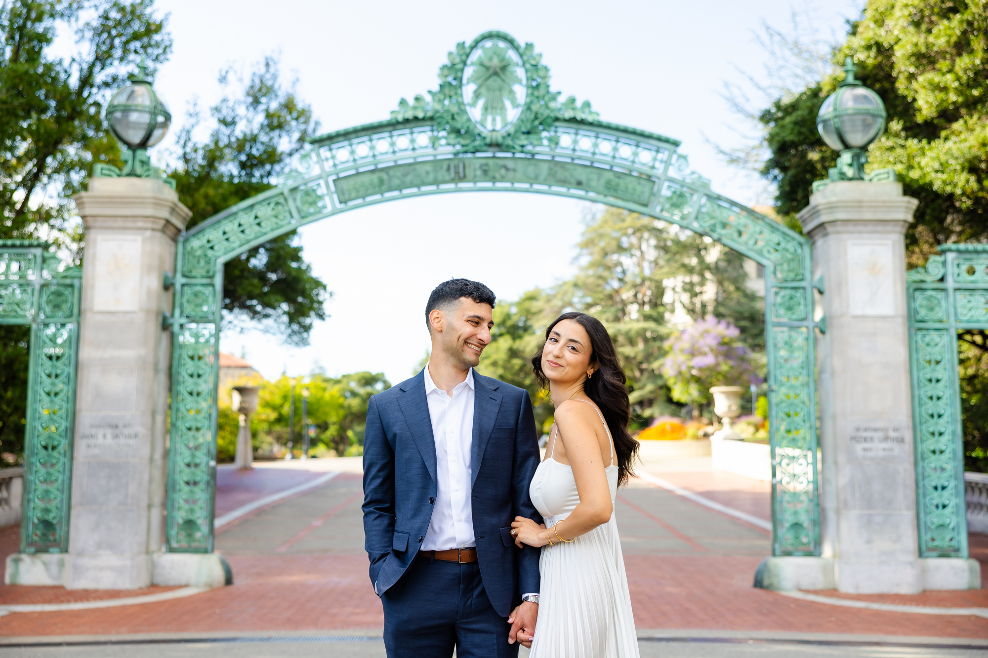 A heterosexual couple stands in front of Sather Gate at UC Berkeley.