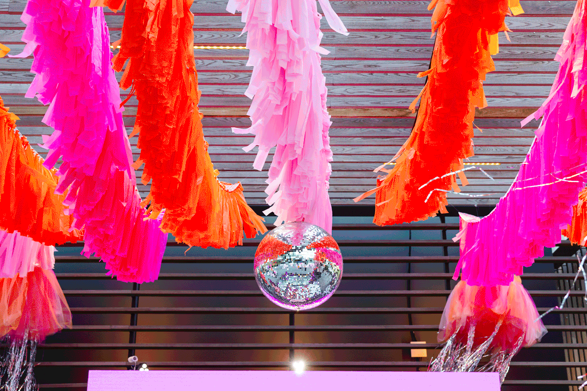 a disco ball spins above a dance floor with pink and orange streamers around it