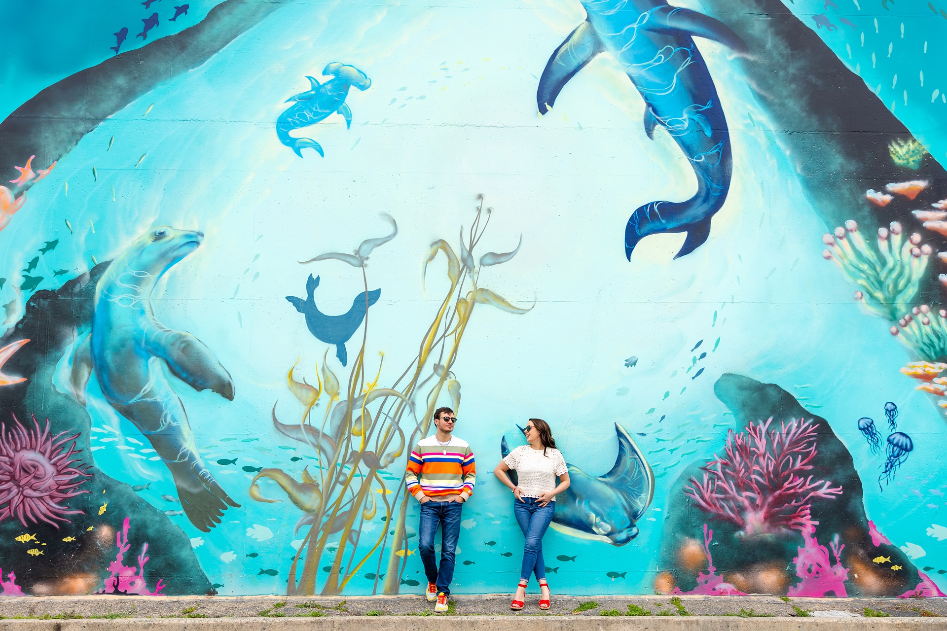 A couple wearing colorful outfits stands in front of an undersea mural during a santa cruz engagement session